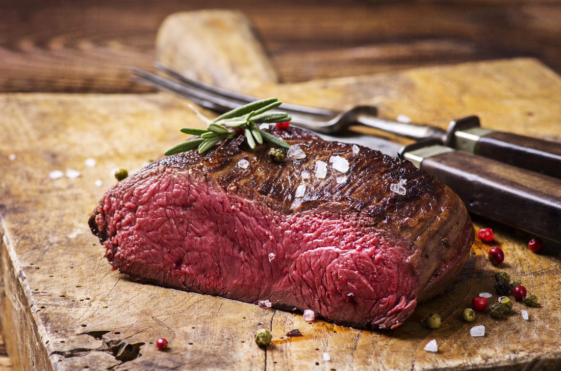 Venison steak cooked medium rare topped with coarse sea salt and rosemary, and tri-color peppercorns.