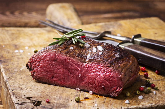 Venison steak cooked medium rare topped with coarse sea salt and rosemary, and tri-color peppercorns.